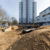 Baustelle mit Erdhügeln und Hochhaus im Hintergrund
