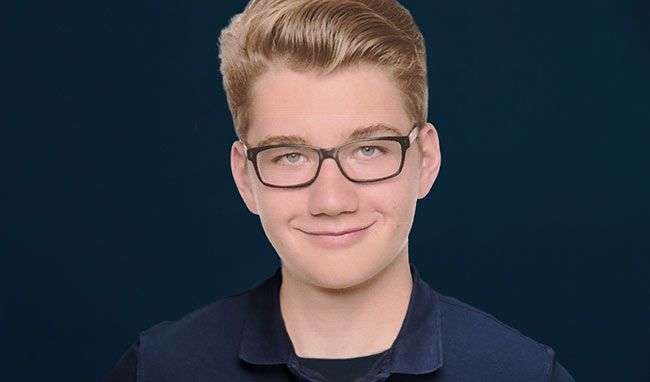 Portraitfoto eines jungen Mannes vor dunkelblauem Hintergrund.