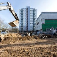Baustelle mit Bagger und Hochhaus im Hintergrund