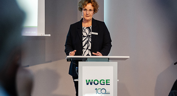 Anja Wiese hinter Rednerpult mit Aufschrift Woge 100 Jahre